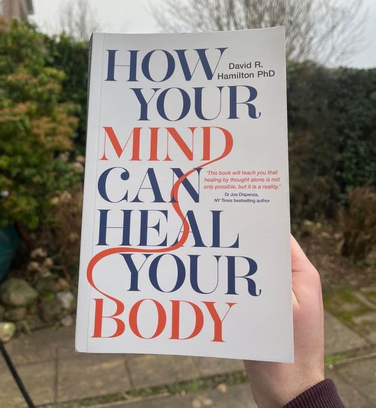 Person wearing headphones while holding an open book in a cozy reading nook