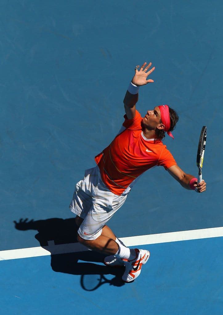 Tennis player serving on a hard court under stadium lights