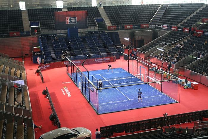 Players competing in a padel tennis match on a glass-walled court
